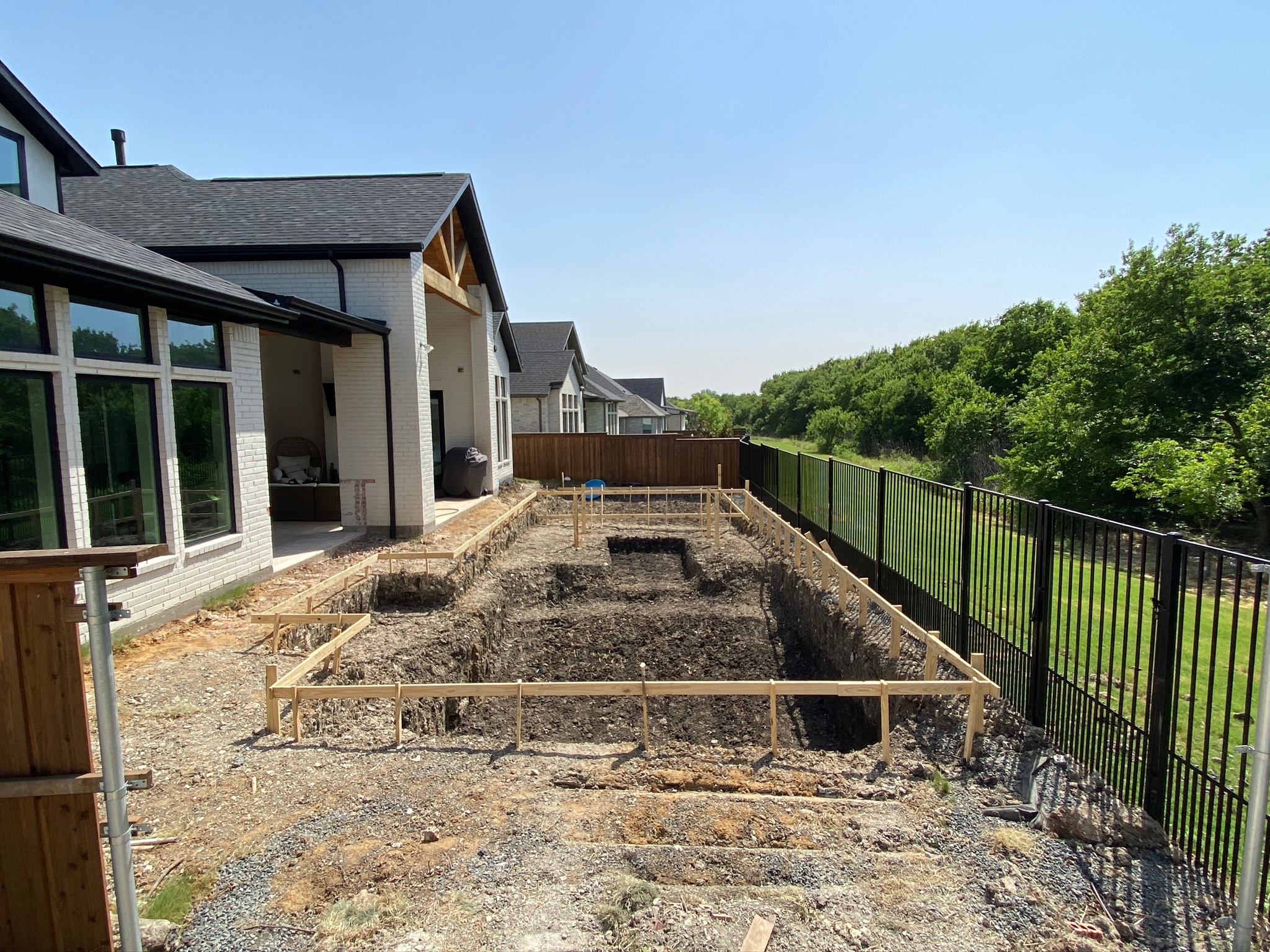 Excavated foundation area beside a modern house under clear sky.