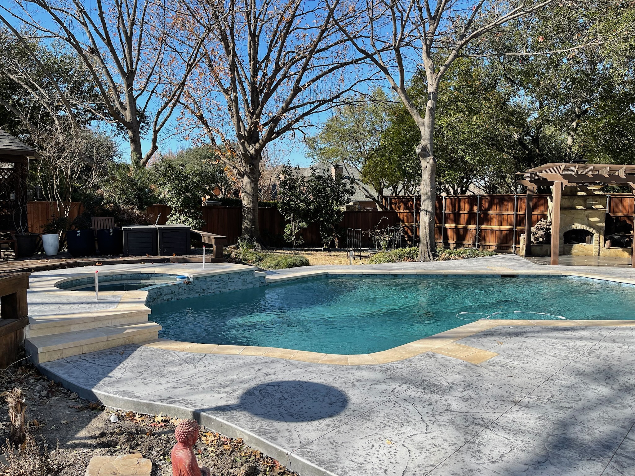 A serene backyard pool surrounded by trees and patio area under a clear blue sky.